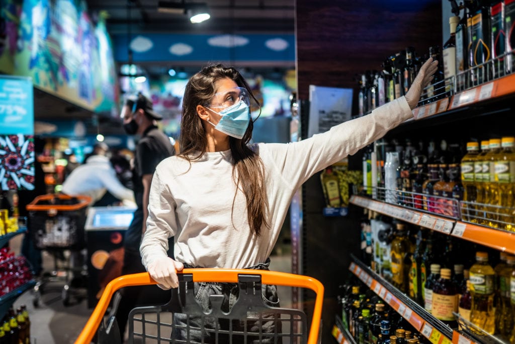 Woman with the surgical mask and the gloves is shopping in the supermarket